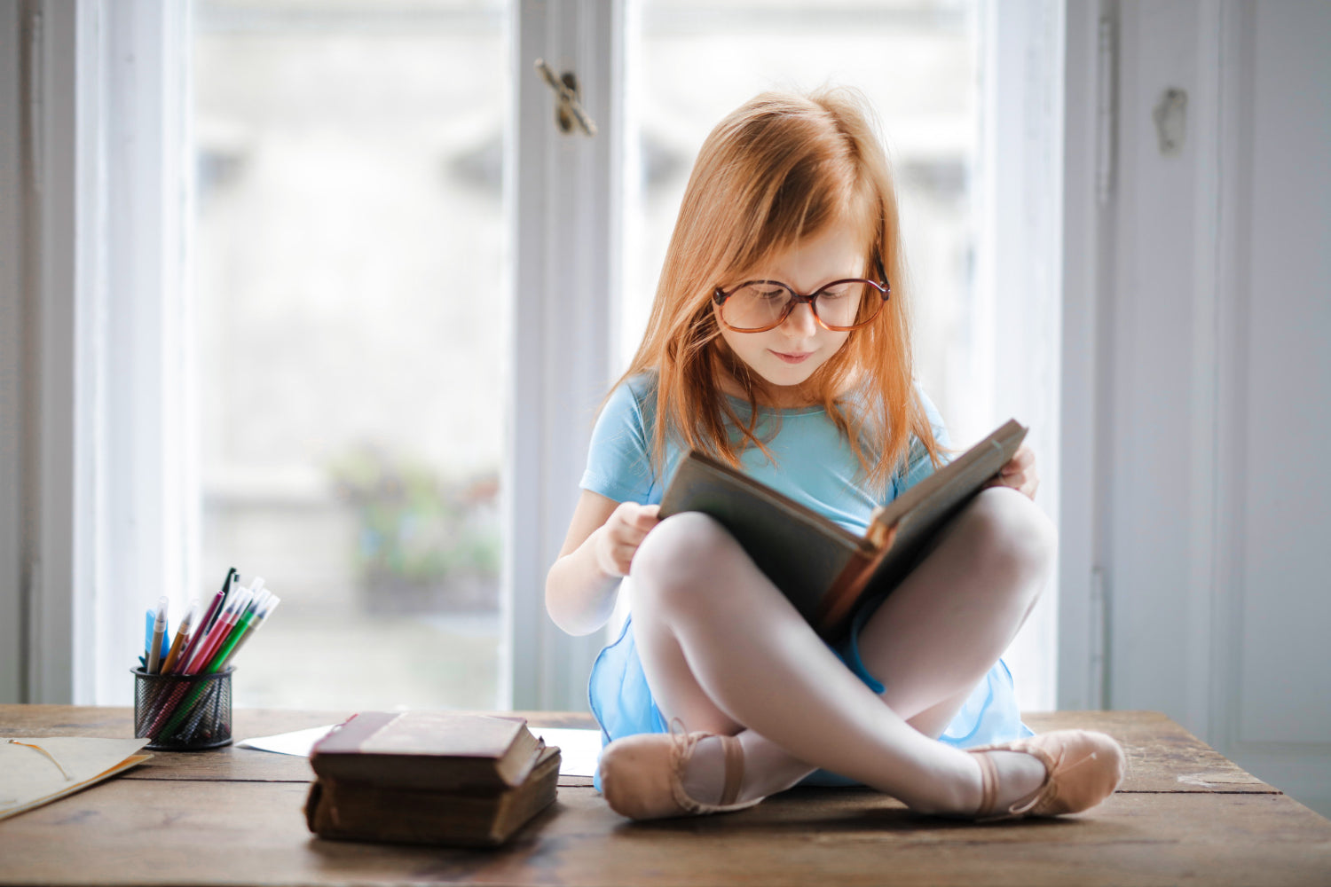 Little girl with glasses reading on top of the table cross legged